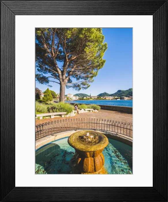 Framed Print : Como, Lombardy, Italy. A fountain on the lake front and a woman reading on a bench Framed Print : Como, Lombardy, Italy. A fountain on the lake front and a woman reading on a bench