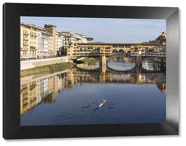 A woman rows on the Arno river towards the Ponte Vecchio, Florence, Tuscany, Italy