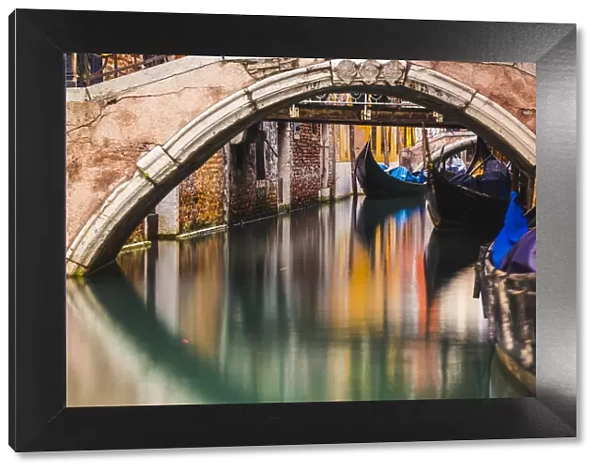 Venice, Veneto, Italy. Moored gondolas under stone bridges