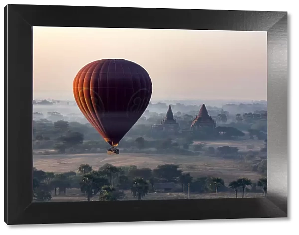 A hot air balloon flies over a temple at sunrise on a misty morning, Bagan, Myanmar