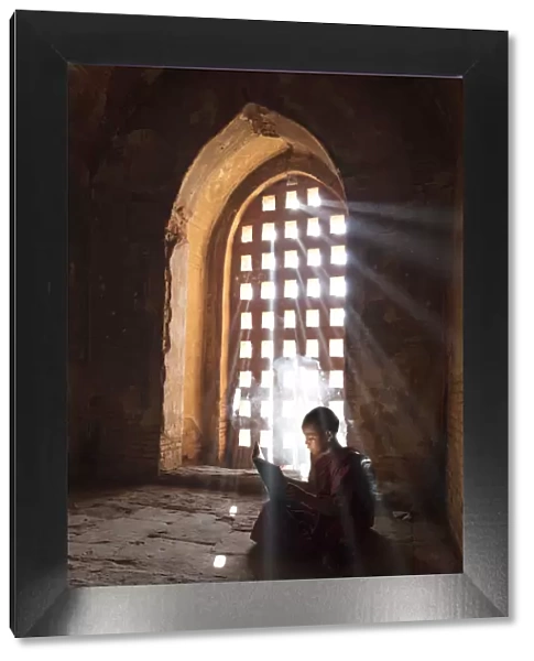 Young Buddhist monk reads by a window in a temple in Bagan, Myanmar