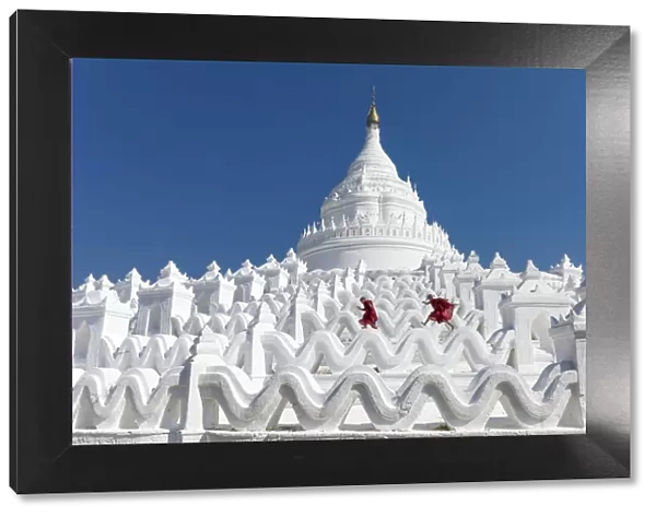 Two young Buddhist monks run and jump across the white walls of Hsinbyume Pagoda, Mingun