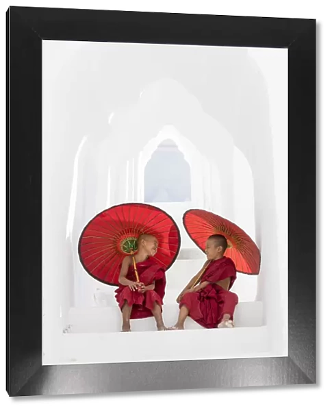 Two young Buddhist monks holding red umbrellas have fun in Hsinbyume Pagoda, Mingun