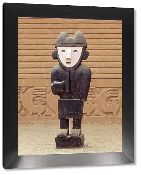South America, Peru, La Libertad, Trujillo, a wooden statue in front of a carved adobe
