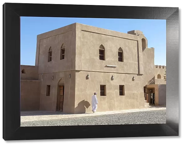 An Omani man walks in front of a restored building in Bahla Fort, Tanuf, Oman