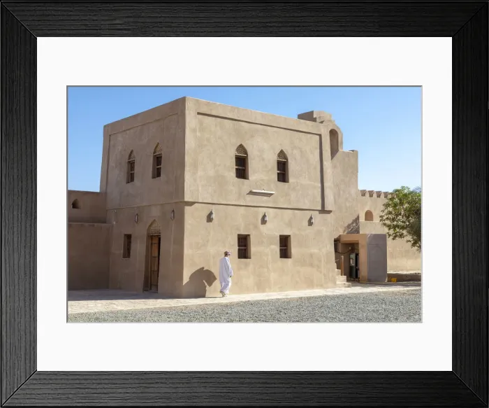 Framed Print : An Omani man walks in front of a restored building in Bahla Fort, Tanuf, Oman
