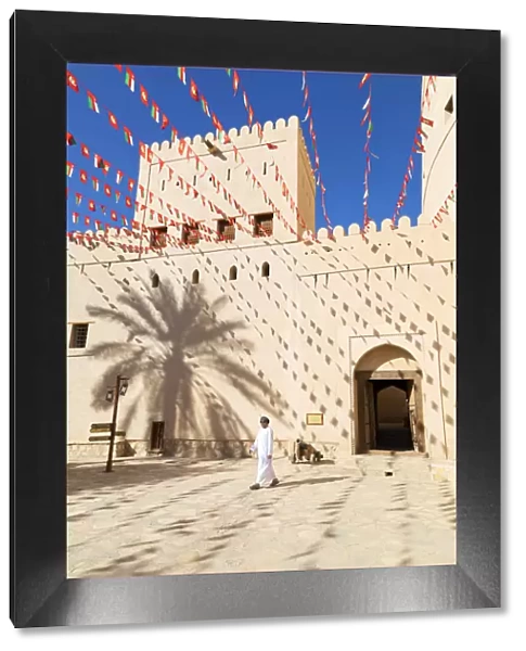 An Omani man walks past Bahla Fort decorated to celebrate the birthday of Sultan Qaboos