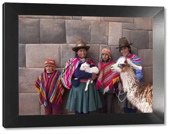 South America, Peru, Cusco. Quechua people standing in front of an Inca wall, holding