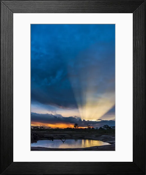 Framed Print : Africa, Zimbabwe, Hwange National park. View across a waterhole at sunbeams bursting Framed Print : Africa, Zimbabwe, Hwange National park. View across a waterhole at sunbeams bursting