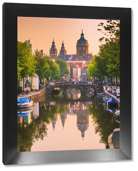 Church of St Nicholas reflecting in the canal at sunrise on a summer evening in Amsterdam