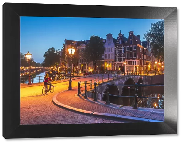 A woman riding a bike by night in Amsterdam along Keizersgracht canal in Amsterdam