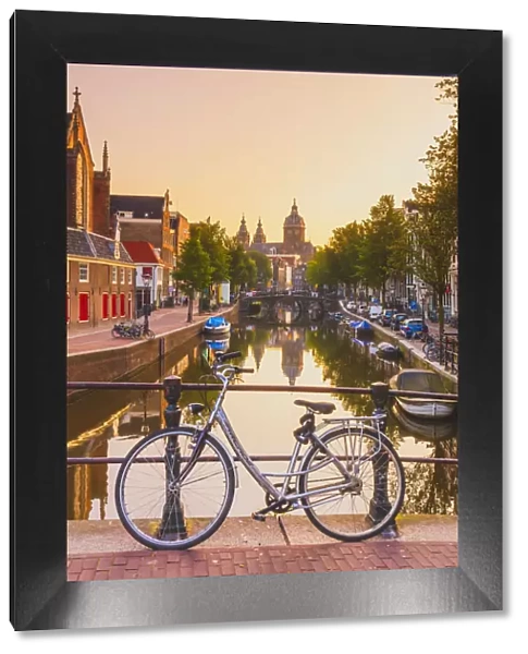 A bike on a bridge with St. Nicholas church in the background at sunrise in Amsterdam