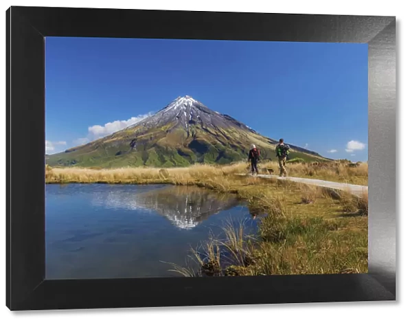Two tourists hiking at Taranaki volcano in New Zealand northern island reflecting in a