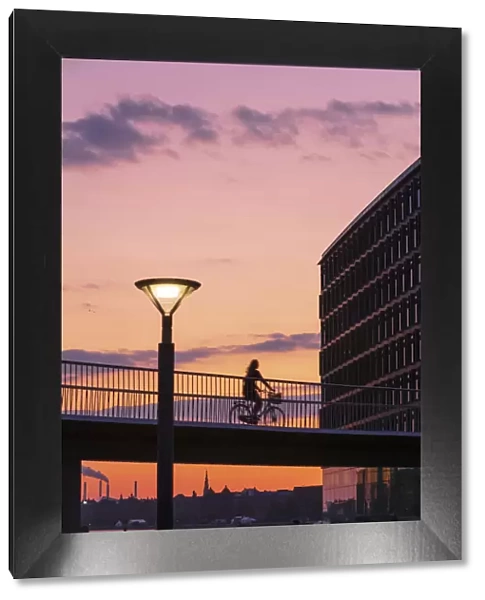 A woman riding a bike on a suspended bridge in Copenhagen at sunset, Denmark