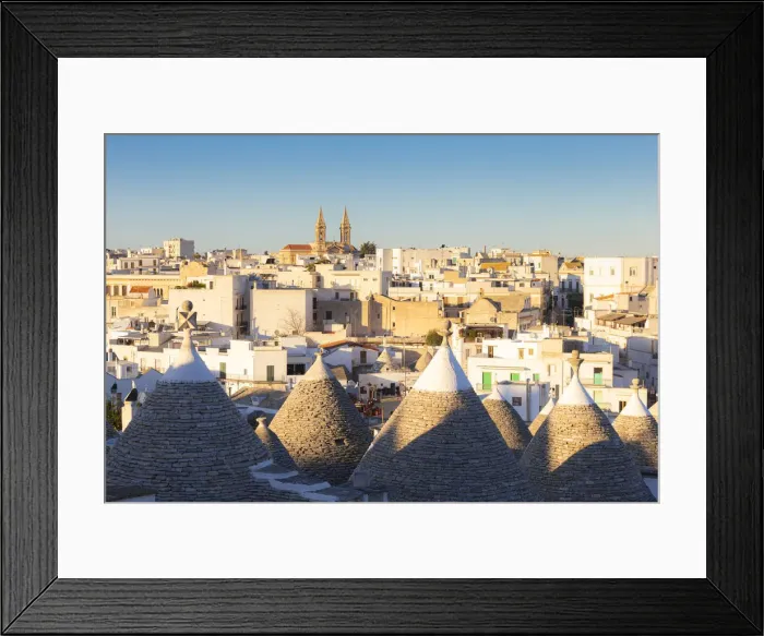 Framed Print : Village of Alberobello illuminated by sun with trulli houses in the foreground Framed Print : Village of Alberobello illuminated by sun with trulli houses in the foreground