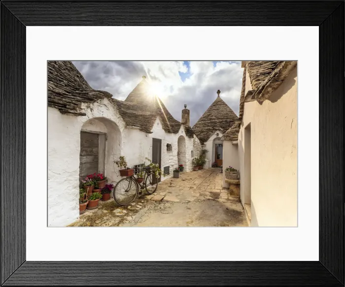 Framed Print : Sun light filters between clouds and illuminates trullo house