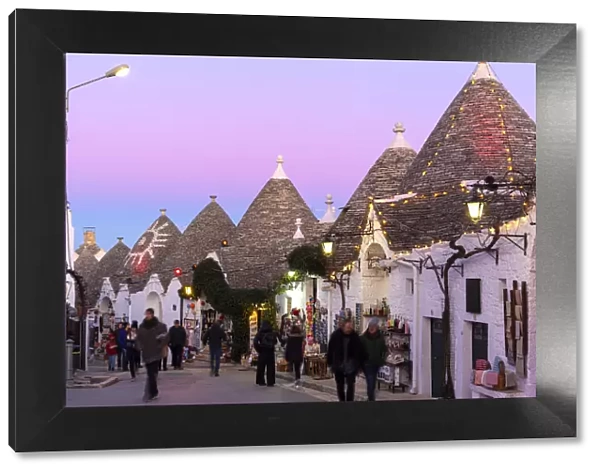 Tourist walks in the pedestrian area between trulli houses at twilight