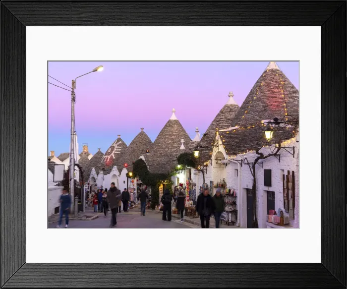 Framed Print : Tourist walks in the pedestrian area between trulli houses at twilight