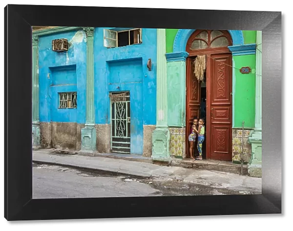 Two young girls peaking through the door of their house in Centro Habana Province, Havana