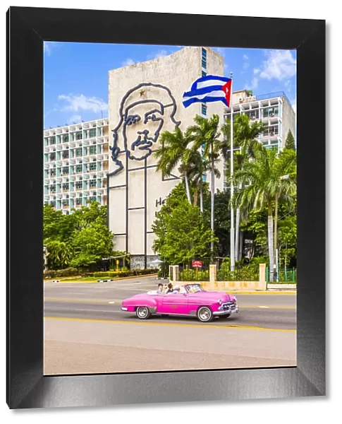 A classic car driving in front of a building with an outline of Che Guevara