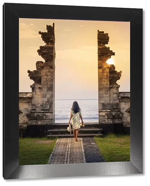 Indonesia, Bali, Candidasa. A young woman walking through the doorway of a traditional