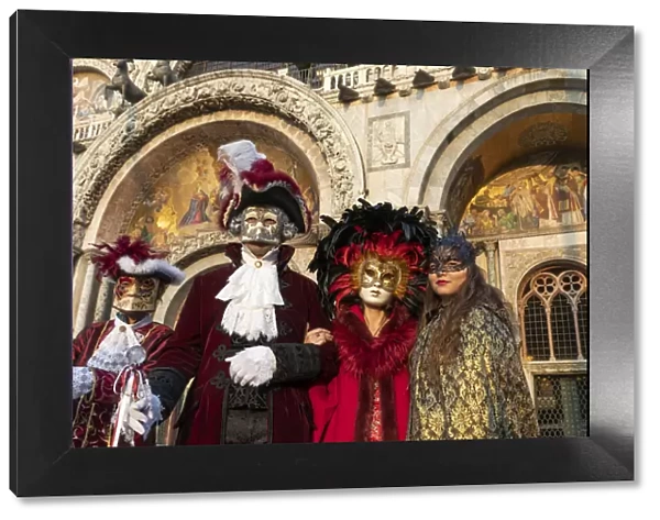 Four people dressed up during the Venice Carnival stand in front of the Basilica in St