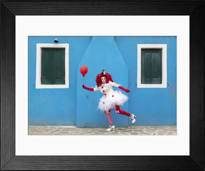 Framed Print : A woman dressed as a clown holds a ballon in front of a colourful facade on Burano Framed Print : A woman dressed as a clown holds a ballon in front of a colourful facade on Burano