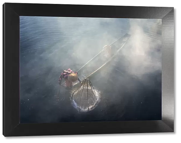 Elevated view of fisherman catching fish from boat using traditional conical net at