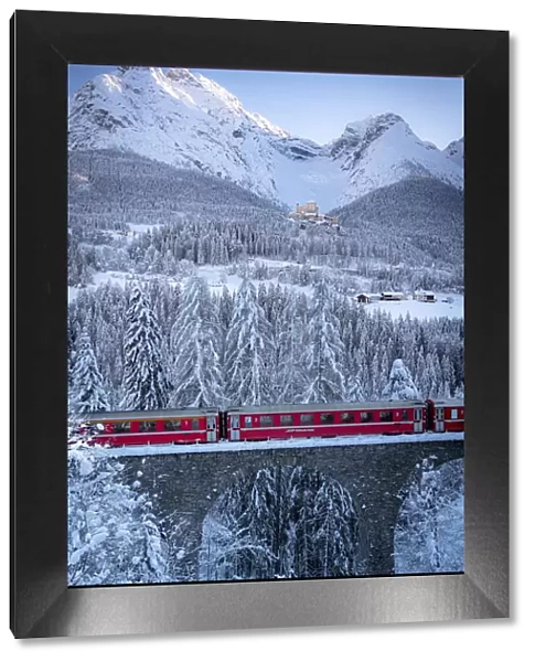 Bernina Express train on viaduct surrounding Tarasp Castle and snow capped mountains