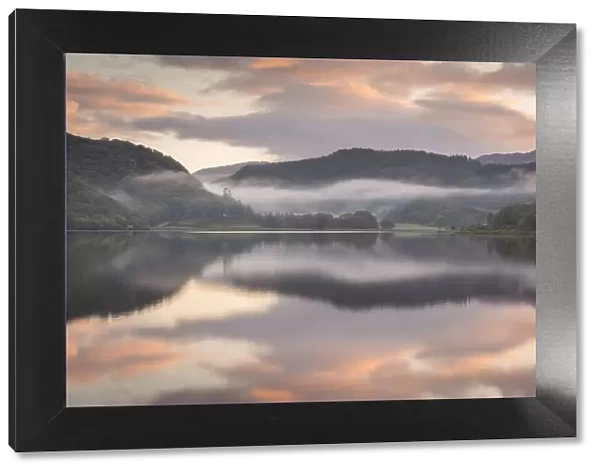 Colourful dawn sky above a reflective and misty Llyn Dinas, Snowdonia National Park