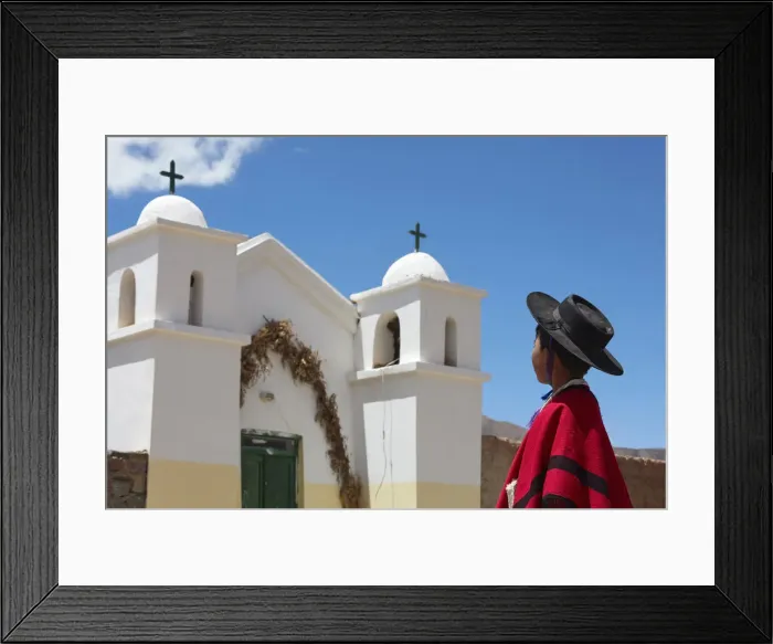 Framed Print : A young Aymara boy wearing traditional clothes stand in front of the small church of Framed Print : A young Aymara boy wearing traditional clothes stand in front of the small church of