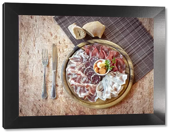 Wood chopping board with mixed italian cold cuts appetizer and cutlery from above