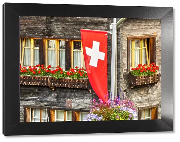 Swiss flag with typical wooden house decorated with flowers behind, Zermatt, Valais