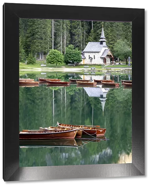 Boats moored in lake Braies (Pragser Wildsee) with small chapel and forest on background