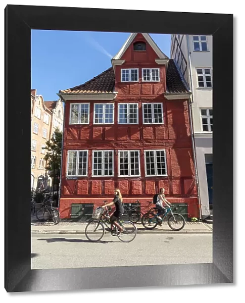 Cyclists pass an old red house in Central Copenhagen, Copenhagen, Denmark