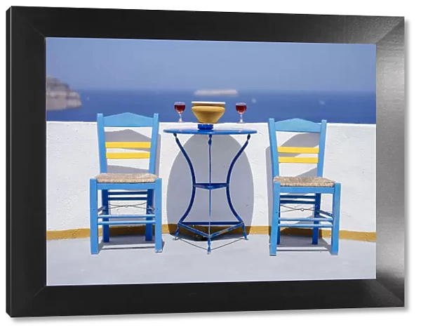 Chairs and table with two glasses of red wine against sea, Santorini, Cyclades