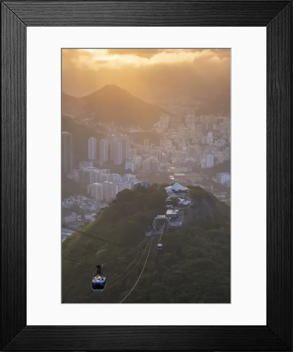 Framed Print : Brazil, Rio de Janeiro, Cable cars ascending to Sugar Loaf mountain. Morro da Urca hill, forest, Rio city in the background under golden light Framed Print : Brazil, Rio de Janeiro, Cable cars ascending to Sugar Loaf mountain. Morro da Urca hill, forest, Rio city in the background under golden light
