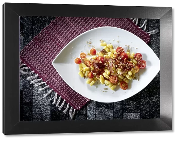 Gnocchi with bacon and small tomatoes on rustic placemat, Italy