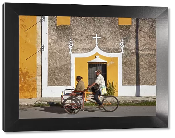 Locals on a tricycle passing by the front facade of a colonial house in Izamal, Yucatan, Mexico