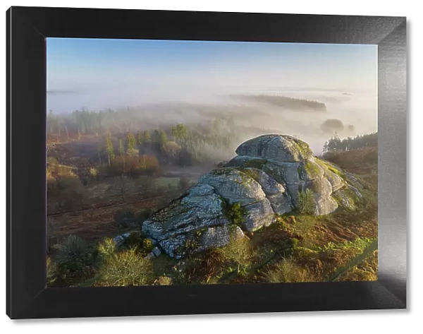 Morning mists swirl around Blackingstone Rock, a granite outcrop in Dartmoor National Park, Devon, England. Winter (March) 2022