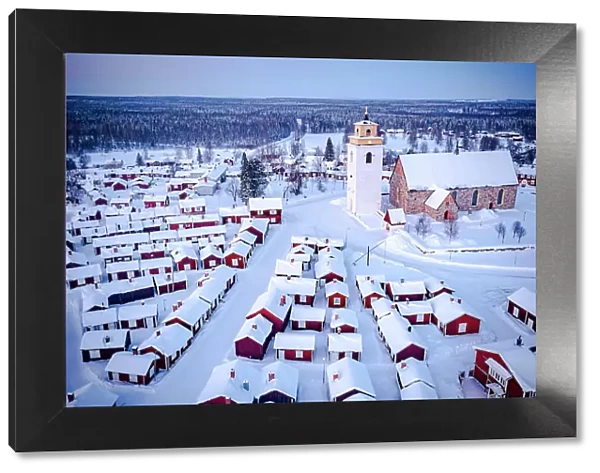 Aerial view of red cabins and church covered with snow at dusk with Lapland forest on background, Gammelstad, Lulea, Sweden