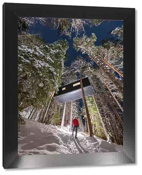 Person admiring the cabin room shaped like a capsule among tall trees in the snowy forest, Tree Hotel, Harads, Lapland, Sweden