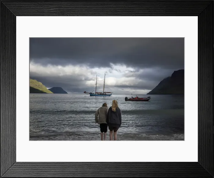 Framed Print : Two girls at G! Festival in Syðrugota walking into the ocean. In the background the sailship Norðlysið. Island of Eysturoy. Faroe Islands
