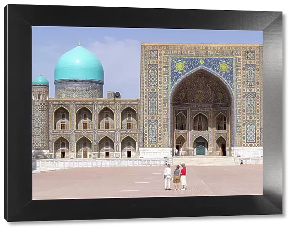 Uzbekistan, Samarkand, Registan square, tourists admire the facade of the Tilya-Kori Madrasah