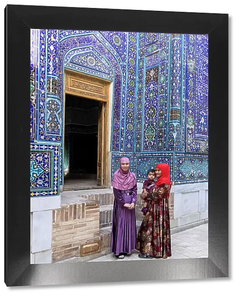 Uzbekistan, Samarkand, Shah-i-Zinda, Tomb Street of 11 Mausoleums, two young women with a baby stand in front of the entrance to a mausoleum