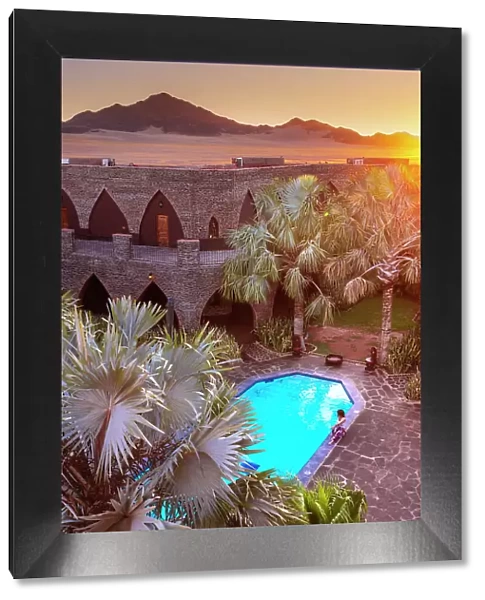 Namibia, a swimming pool in a luxury hotel in the Namib Naukluft National Park with the sun setting on the Namib desert dunes