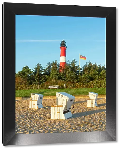 Beach chairs near German flag and Hornum lighthouse in background at sunrise, Hornum beach, Sylt, Nordfriesland, Schleswig-Holstein, Germany