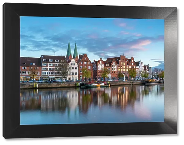 Houses on riverfront of Trave river with towers of St. Marienkirche church in background at sunset, Lubeck, UNESCO, Schleswig-Holstein, Germany