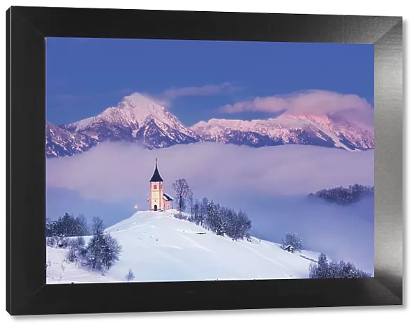 Slovenia, Jamnik, Church of St. Primoz sorrounded by fog at dusk with the Kamnik-Savinja Alps beyond, Gorenjska