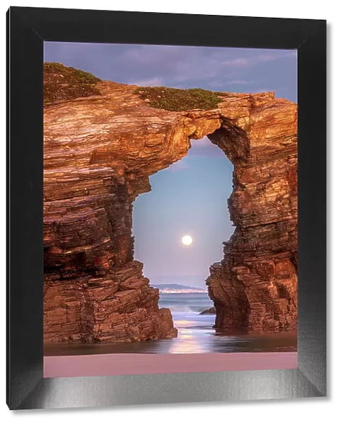 Moon thorugh a natural arch at Playa As Catedrais, Bay of Biscay, Costa Verde, Spain